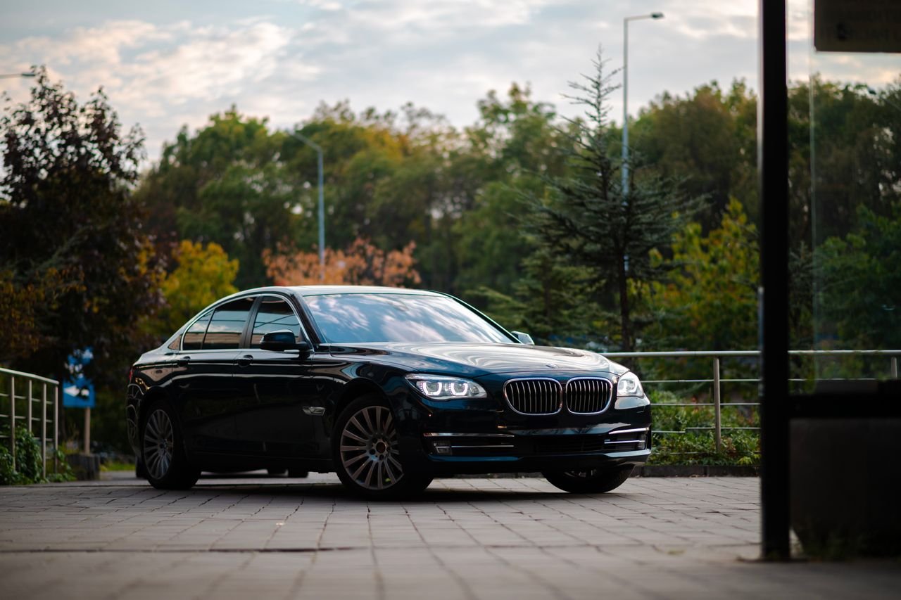 Elegant black sedan parked on pavement with green foliage background on a sunny day.